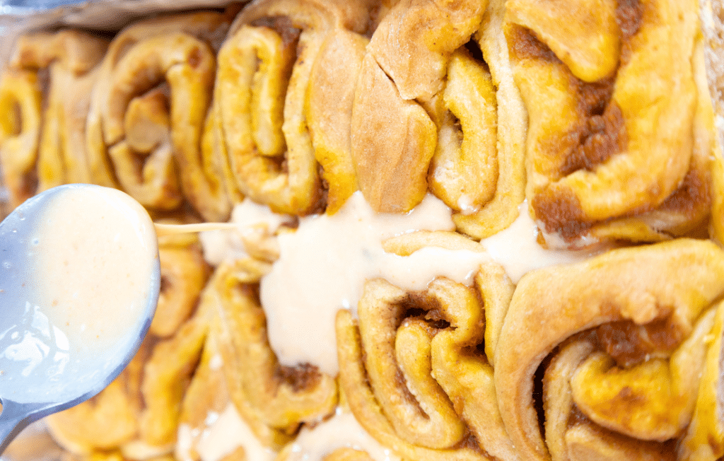 delicious pumpkin cinnamon rolls Drizzling icing on cinnamon rolls