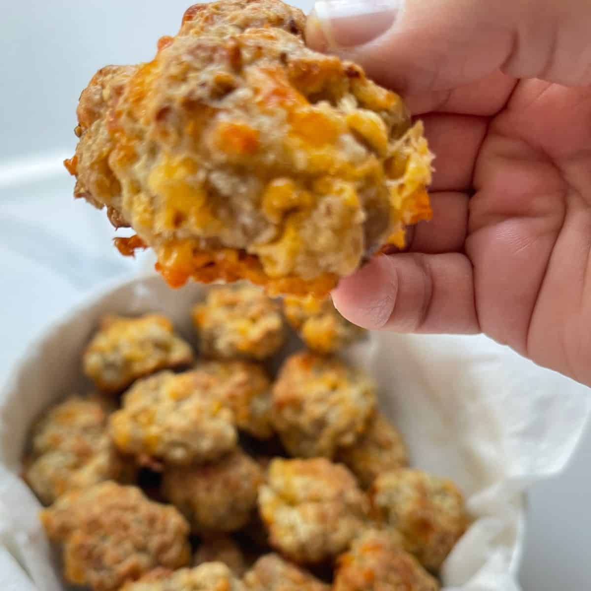 Sausage and cream cheese balls A hand holding a large sausage ball over a bowl of sausage balls