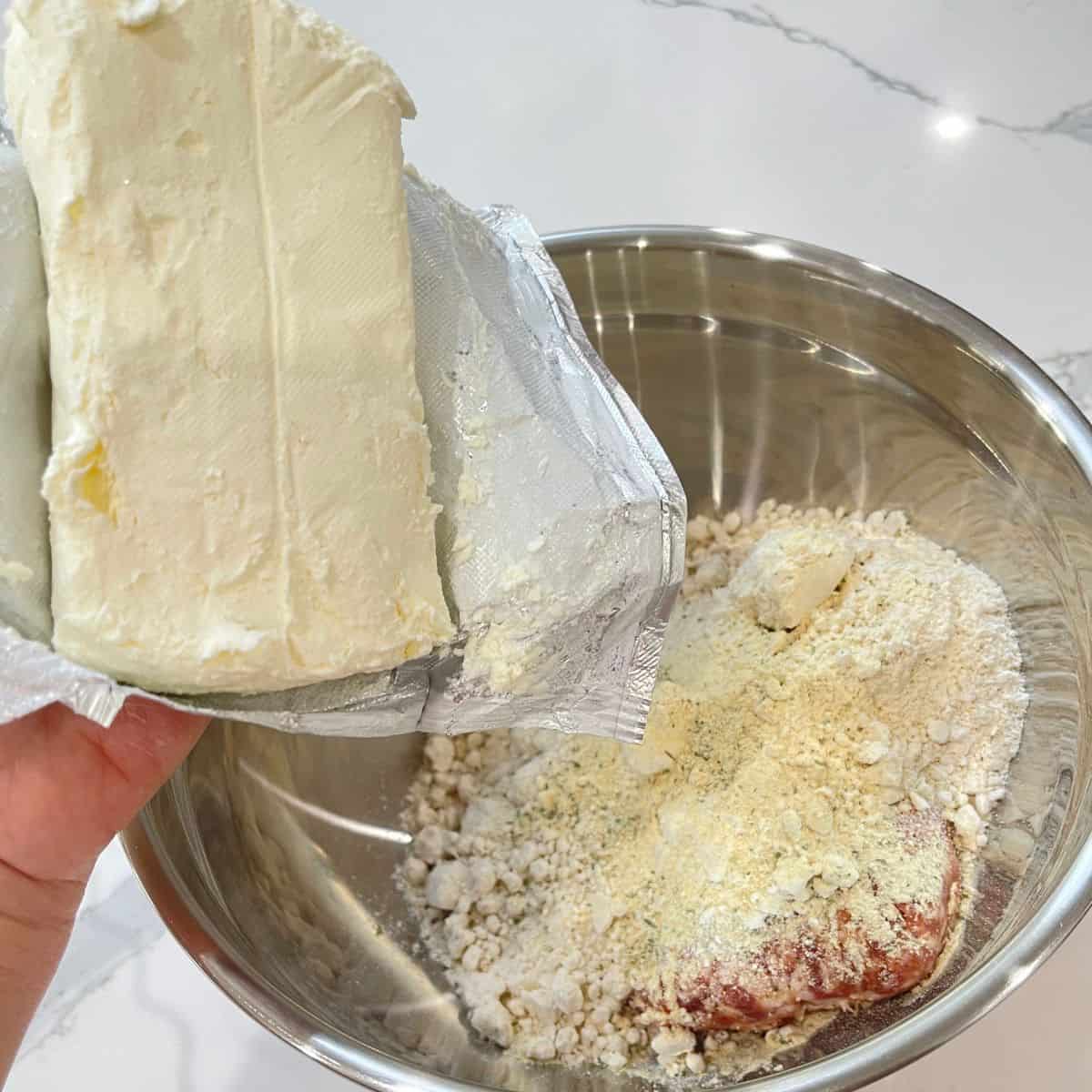A silver bowl with cream cheese and sausage ball ingredients