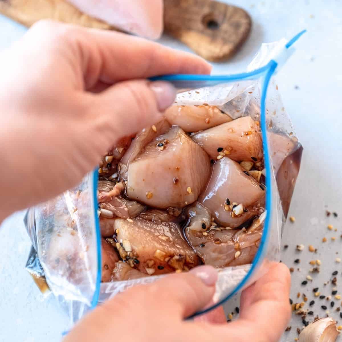 Freezer meals save time and money a person placing raw, cut-up chicken inside a ziplock bag for freezing.