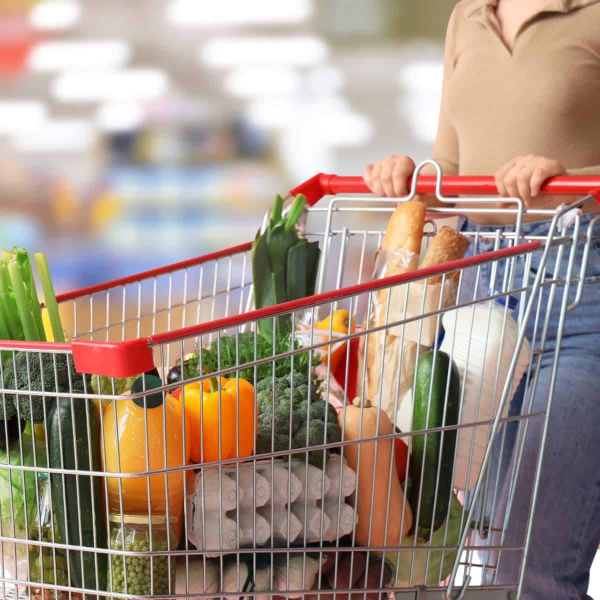Buy groceries on a budget A woman pushing a grocery cart with produce and other items inside
