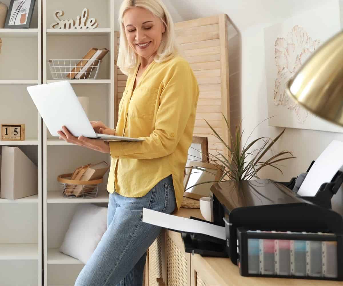 A woman in her home office printing out a document a woman with a yellow shirt using her computer and printing out a PDF at home
