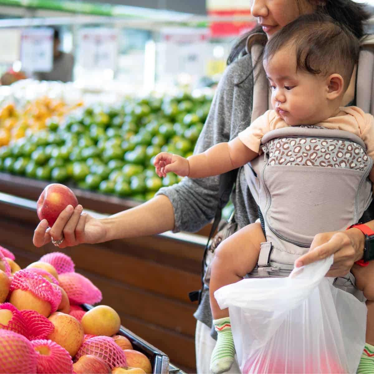 Shopping for cheap groceries A woman holding her baby while shopping for apples