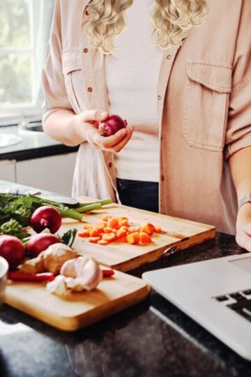 WP Recipe Maker Review for Food Bloggers, woman cutting vegetables in her kitchen and using her computer.