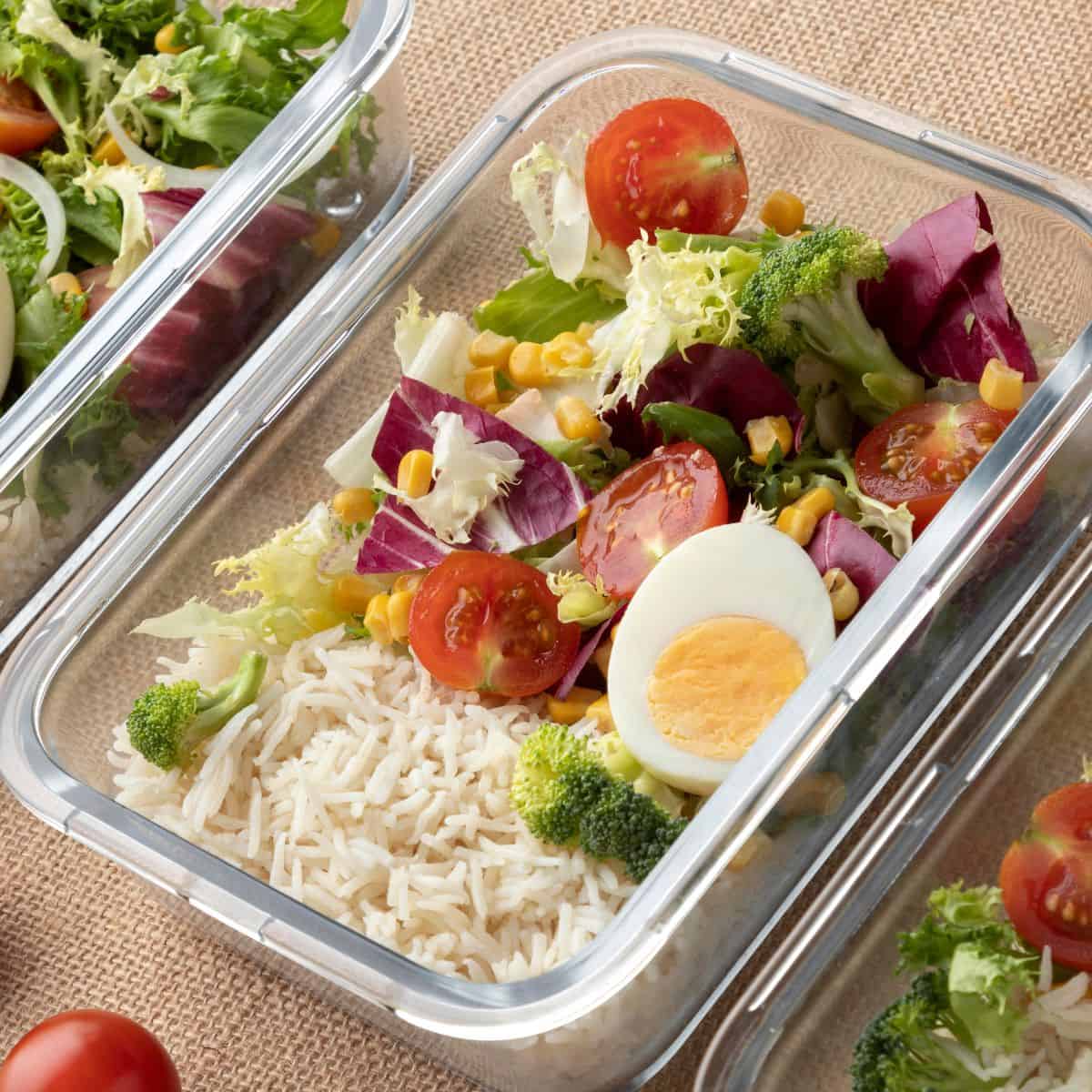 Fresh vegetable salad with rice and boiled egg in glass meal prep container.