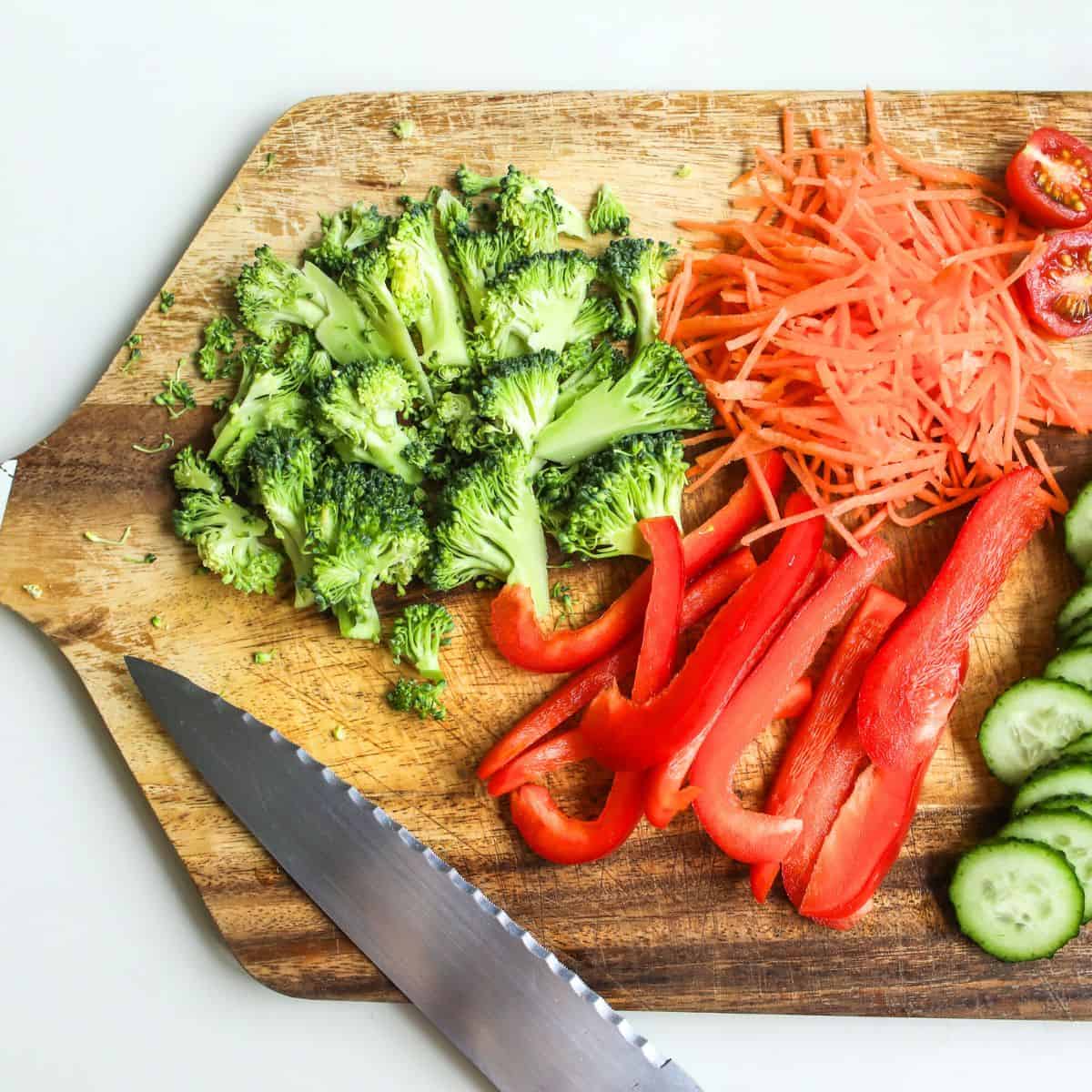 Brightly colored broccoli, red bell peppers, shredded carrots, cherry tomatoes, and cucumber slices.